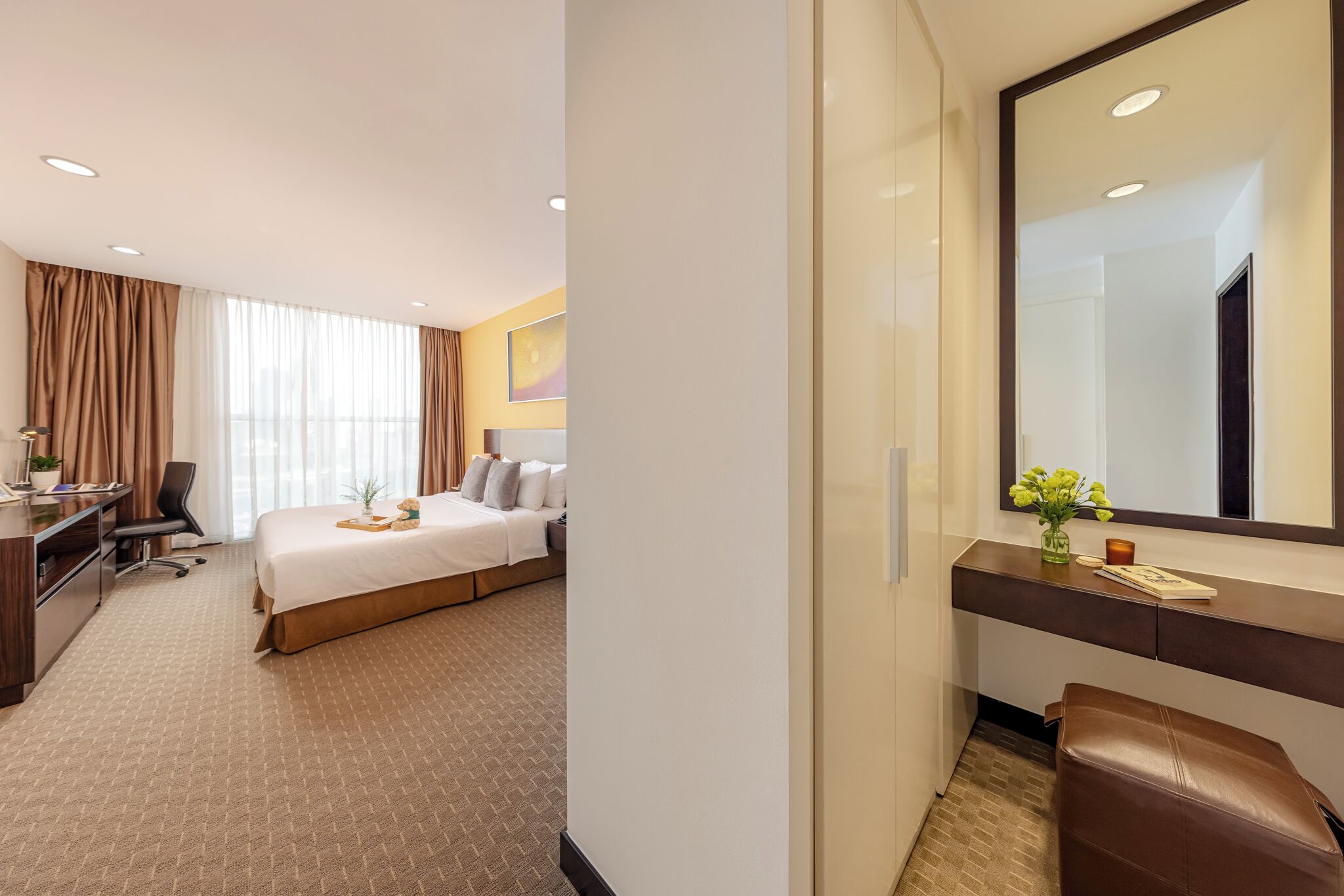 Una habitación de hotel con cama, escritorio, silla y un espejo grande.