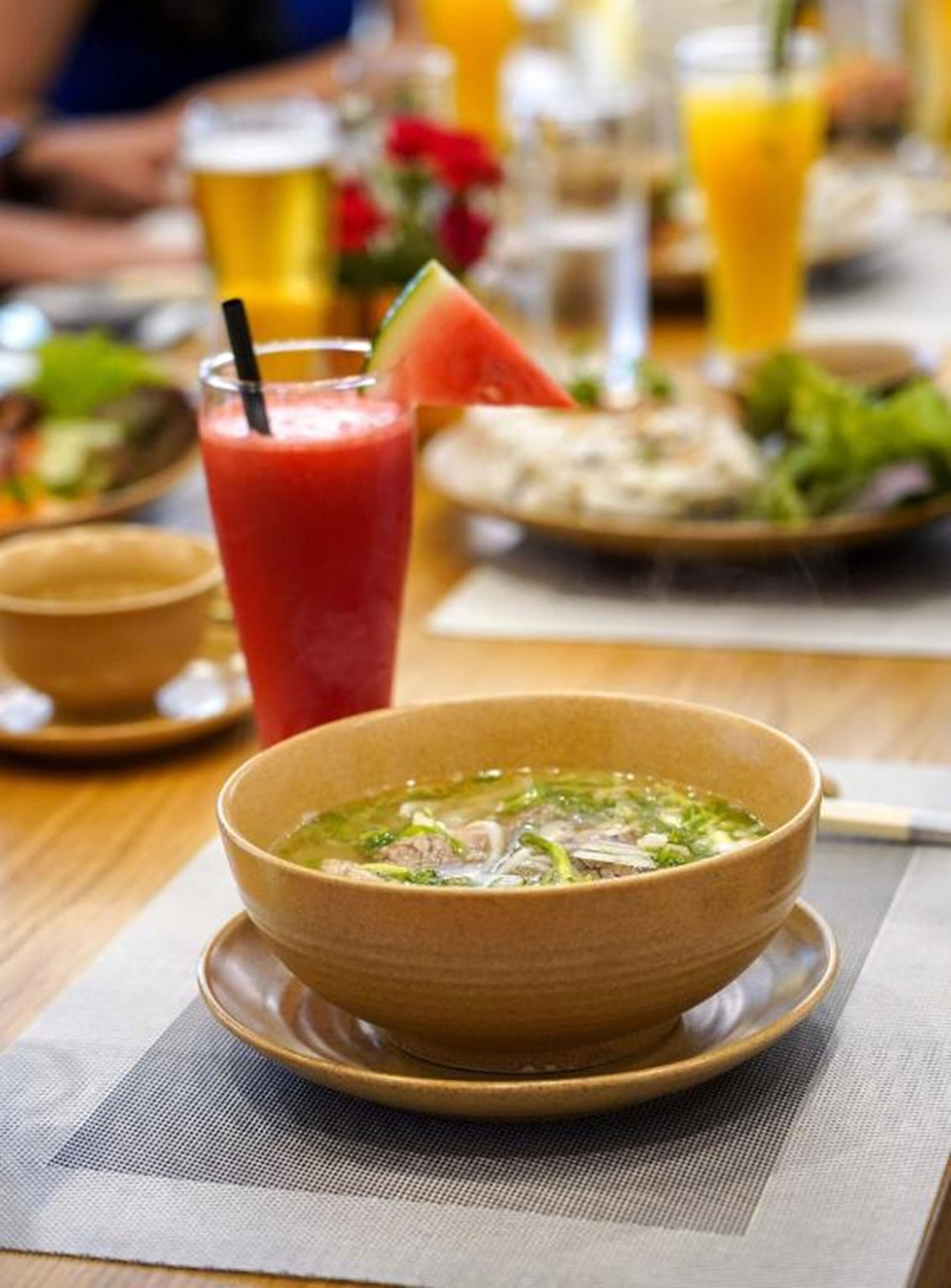 A dining table with a bowl of soup, a glass of red drink, and a plate of food.