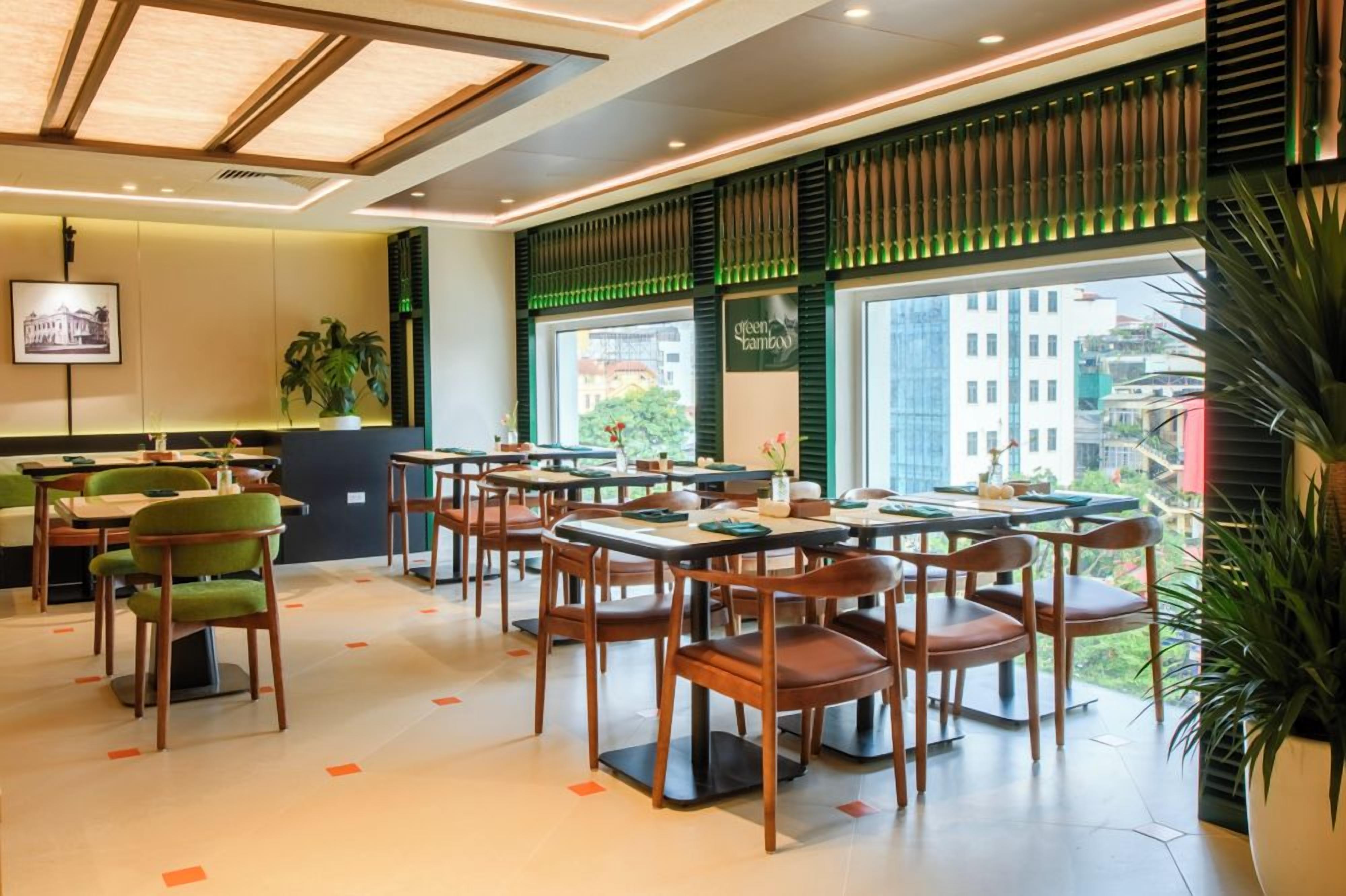 A restaurant with multiple tables and chairs, large windows, and indoor plants.