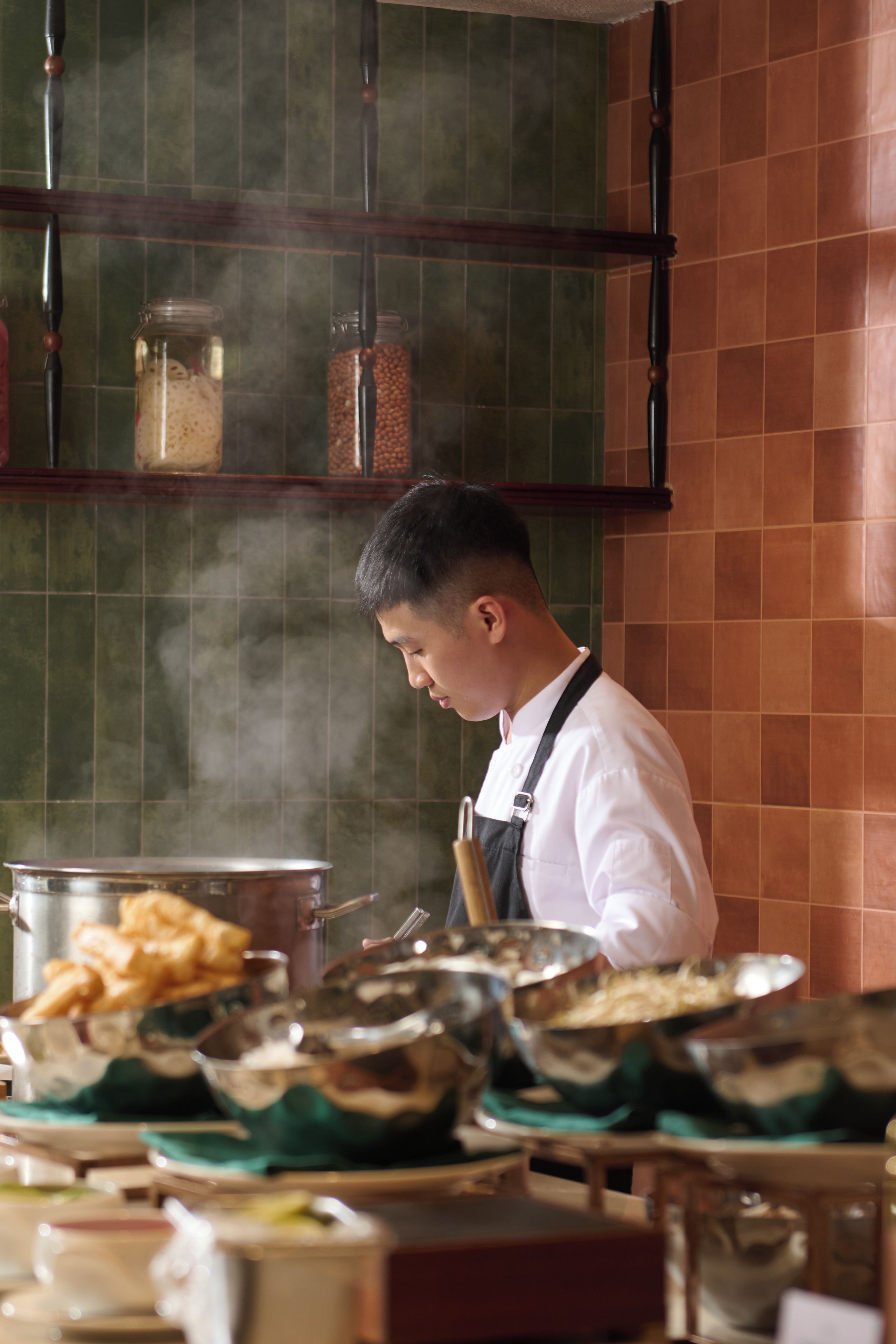 Un cocinero en una cocina con estufa, ollas y diversos alimentos.