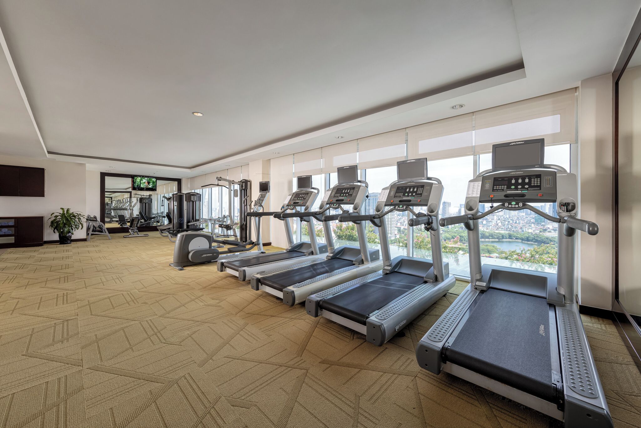 Un gimnasio con cintas de correr, máquinas de ejercicio y amplios ventanales con vistas a la ciudad.