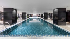 A modern indoor pool with clear water, surrounded by dark-toned walls and a tiled floor.