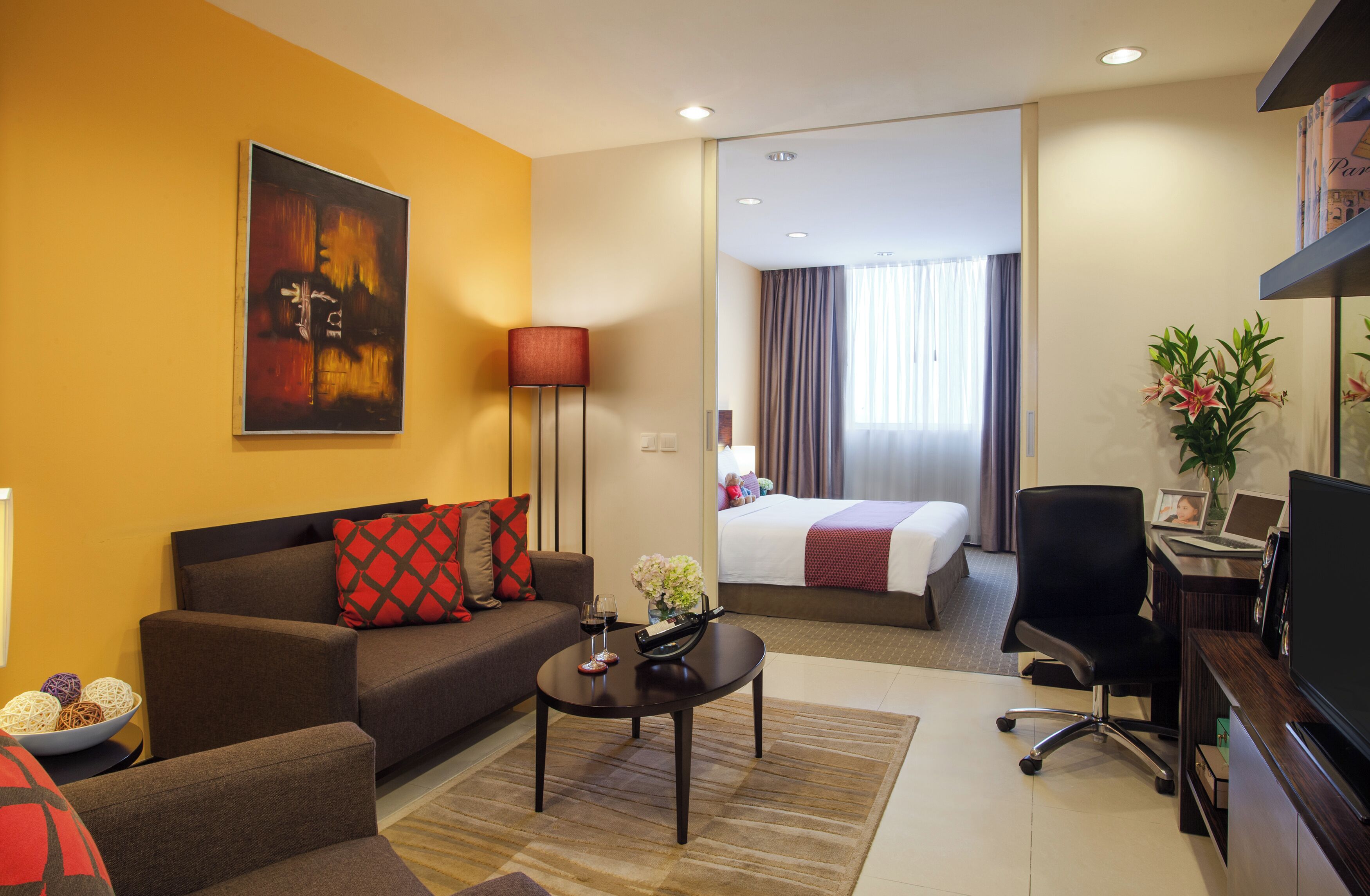 Une chambre d’hôtel comprenant un canapé, une table basse, un bureau avec une chaise, un lit, une télévision et un tableau au mur.