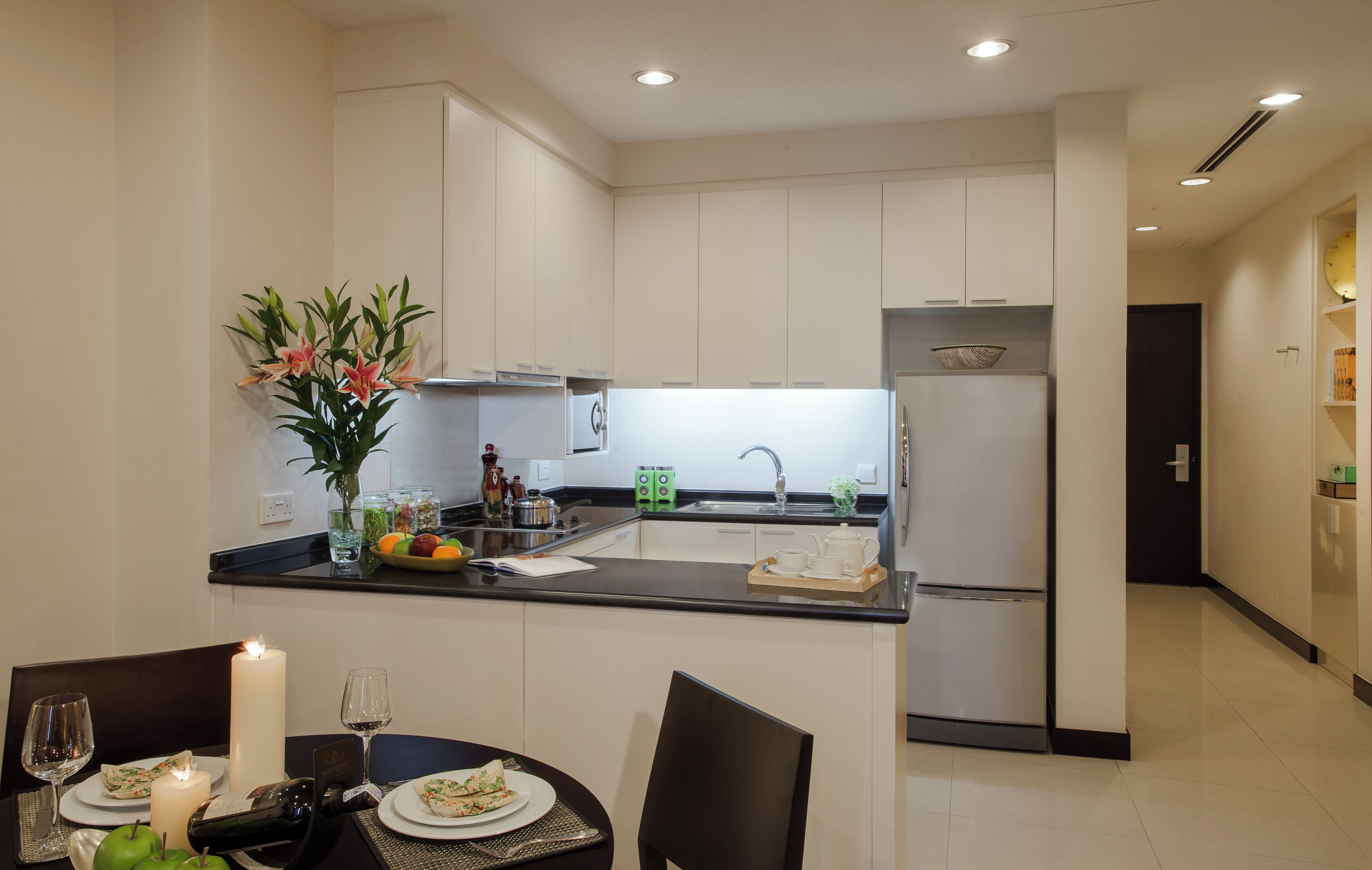 Une cuisine moderne avec des meubles blancs, un plan de travail noir et un coin repas avec une table dressée pour deux personnes.