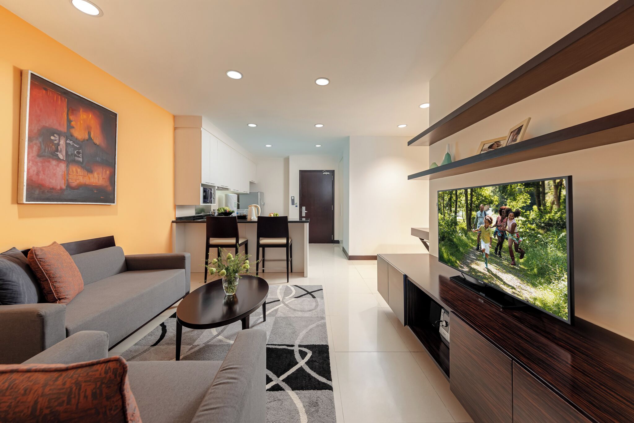 A modern living room with a sofa, coffee table, and TV. A kitchen is visible in the background.