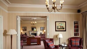 A room with a fireplace, a chandelier, a bookshelf, and two leather armchairs. - Burythorpe House (Malton)