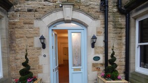 A stone building entrance with a white door, two wooden planters with flowers, and a sign reading "Yorkshire Life". - Burythorpe House (Malton)