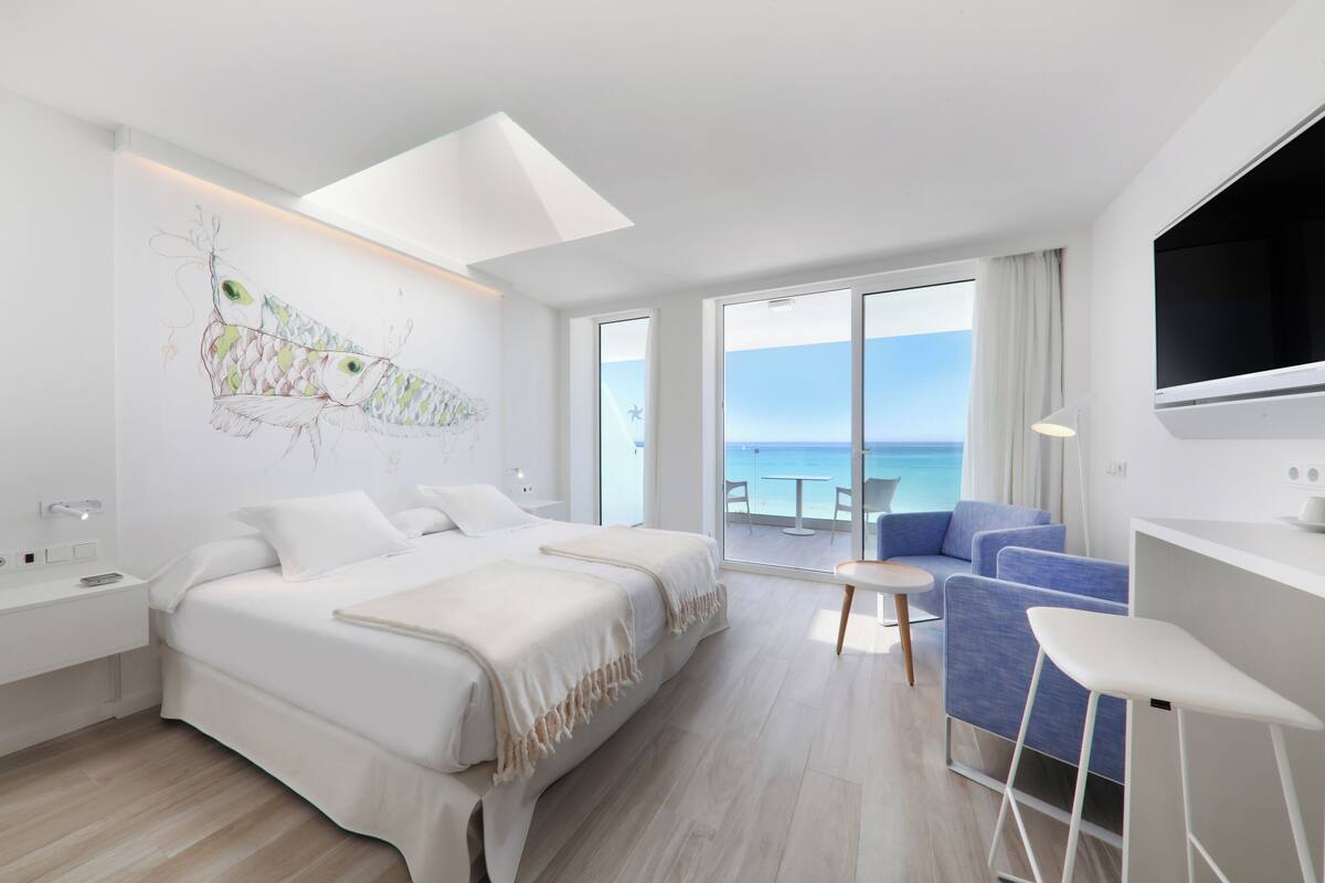 Ein modernes Hotelzimmer mit Bett, Schreibtisch, blauem Sofa und großem Fenster mit Meerblick.