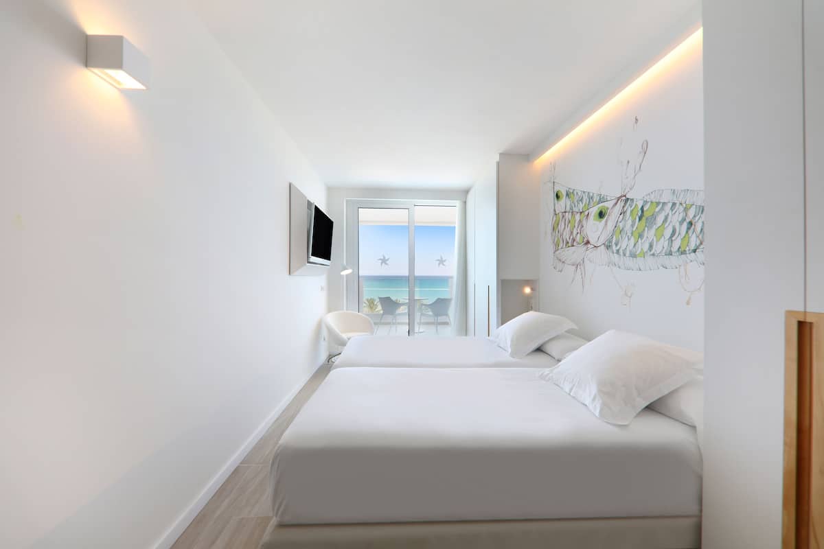 Ein modernes Hotelzimmer mit zwei Betten, einem Fernseher und einem Balkon mit Meerblick.