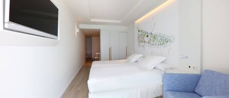 A modern hotel room with two beds, a blue sofa, a large window, and a wall-mounted artwork.