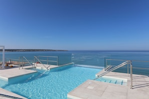 En pool med kristallklart blått vatten, en glasvägg och utsikt över havet.