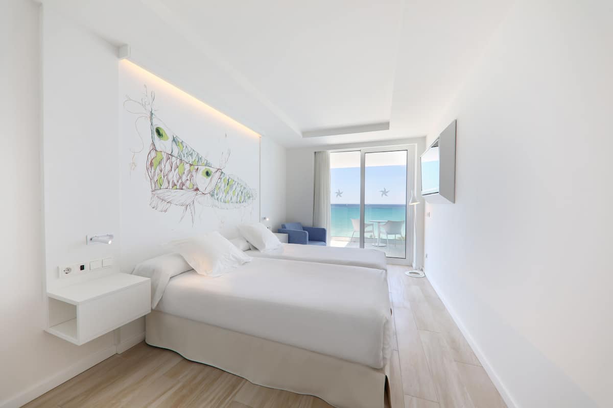 Ein modernes Hotelzimmer mit einem großen Bett, einem Nachttisch, einem an der Wand montierten Fernseher und einem Balkon mit Meerblick.