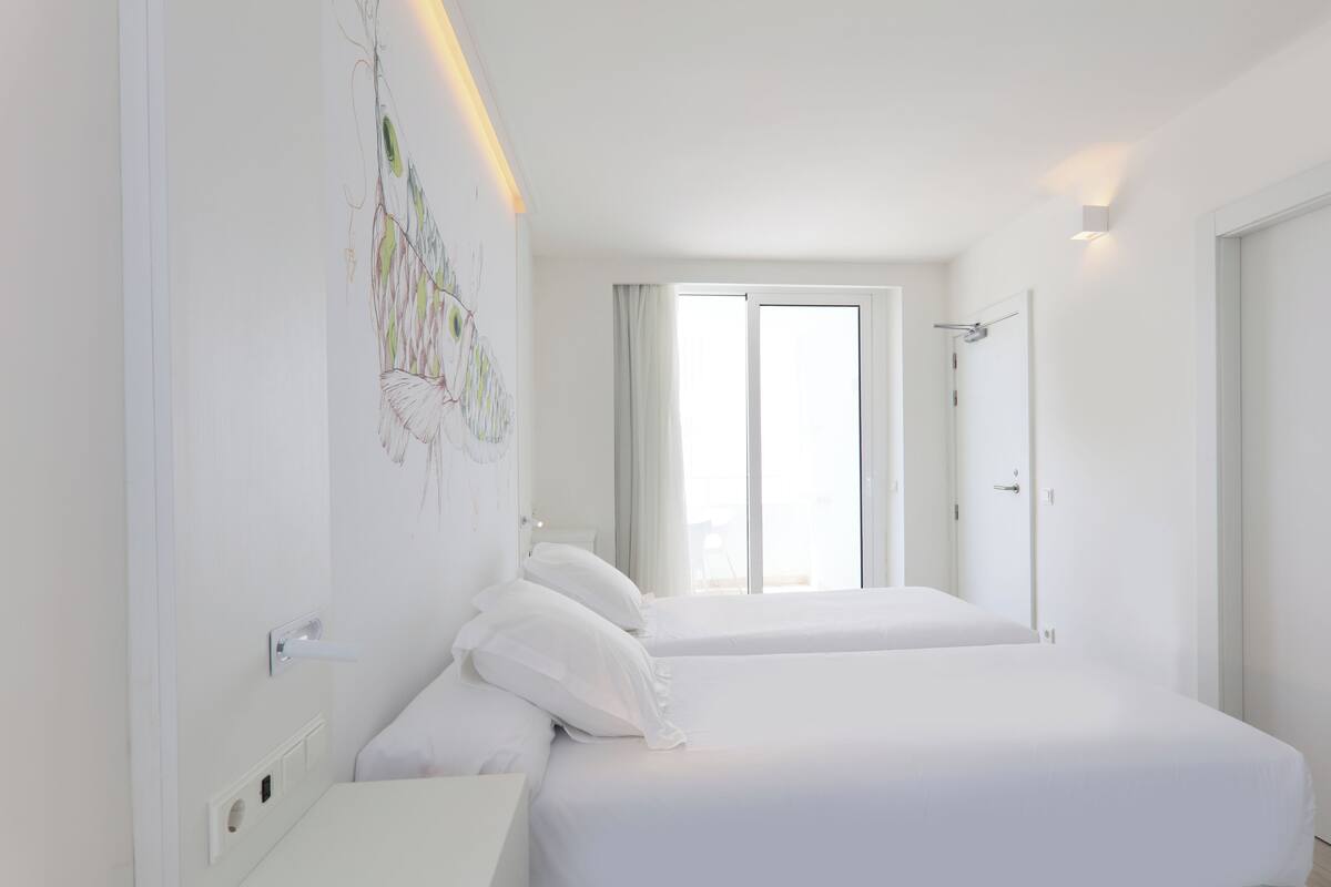 Ein Hotelzimmer mit zwei Betten, einem großen Fenster und einem an der Wand hängenden Kunstwerk.