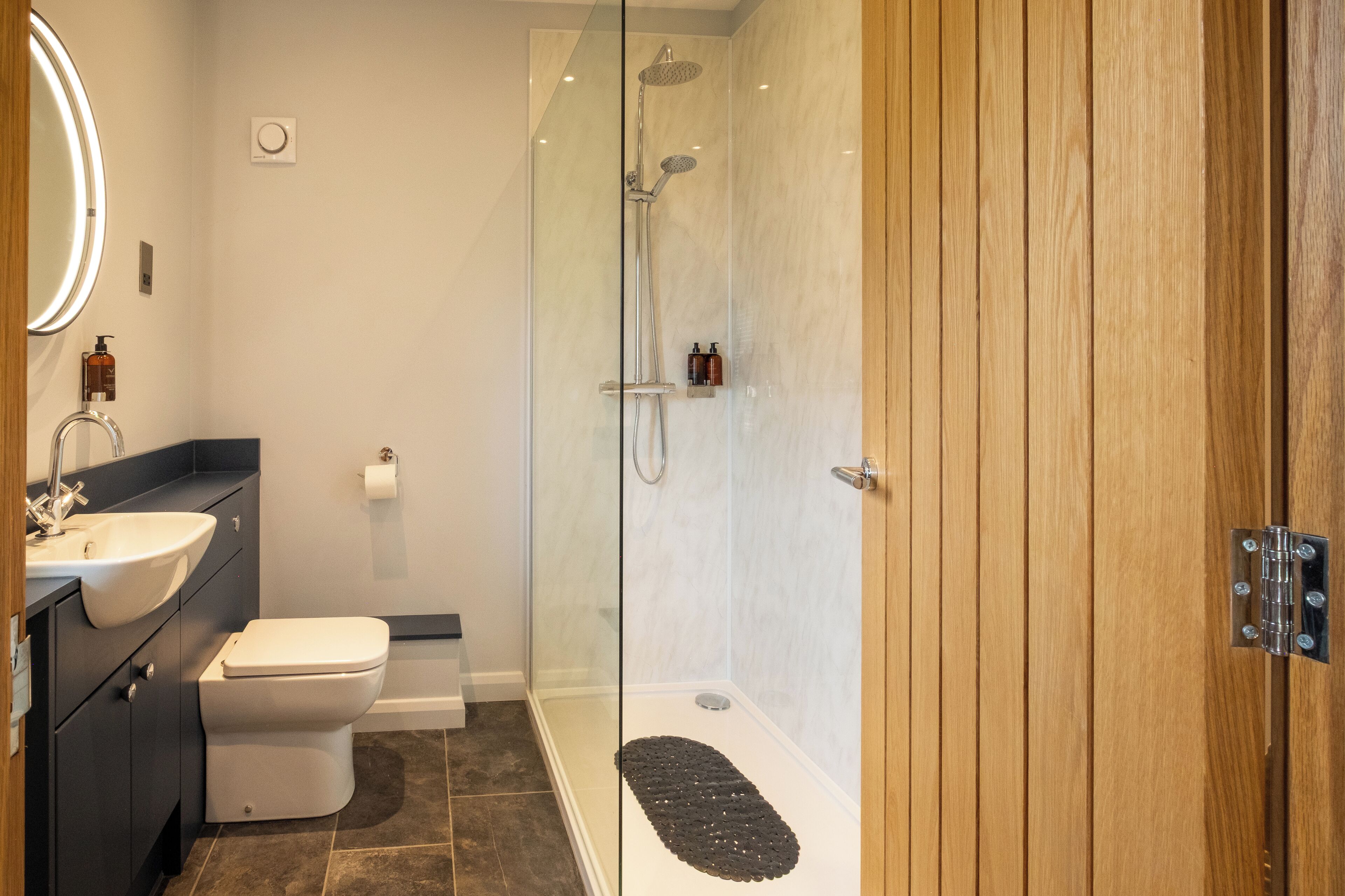 A modern bathroom with a glass-enclosed shower, a white toilet, a sink, and a wooden door.