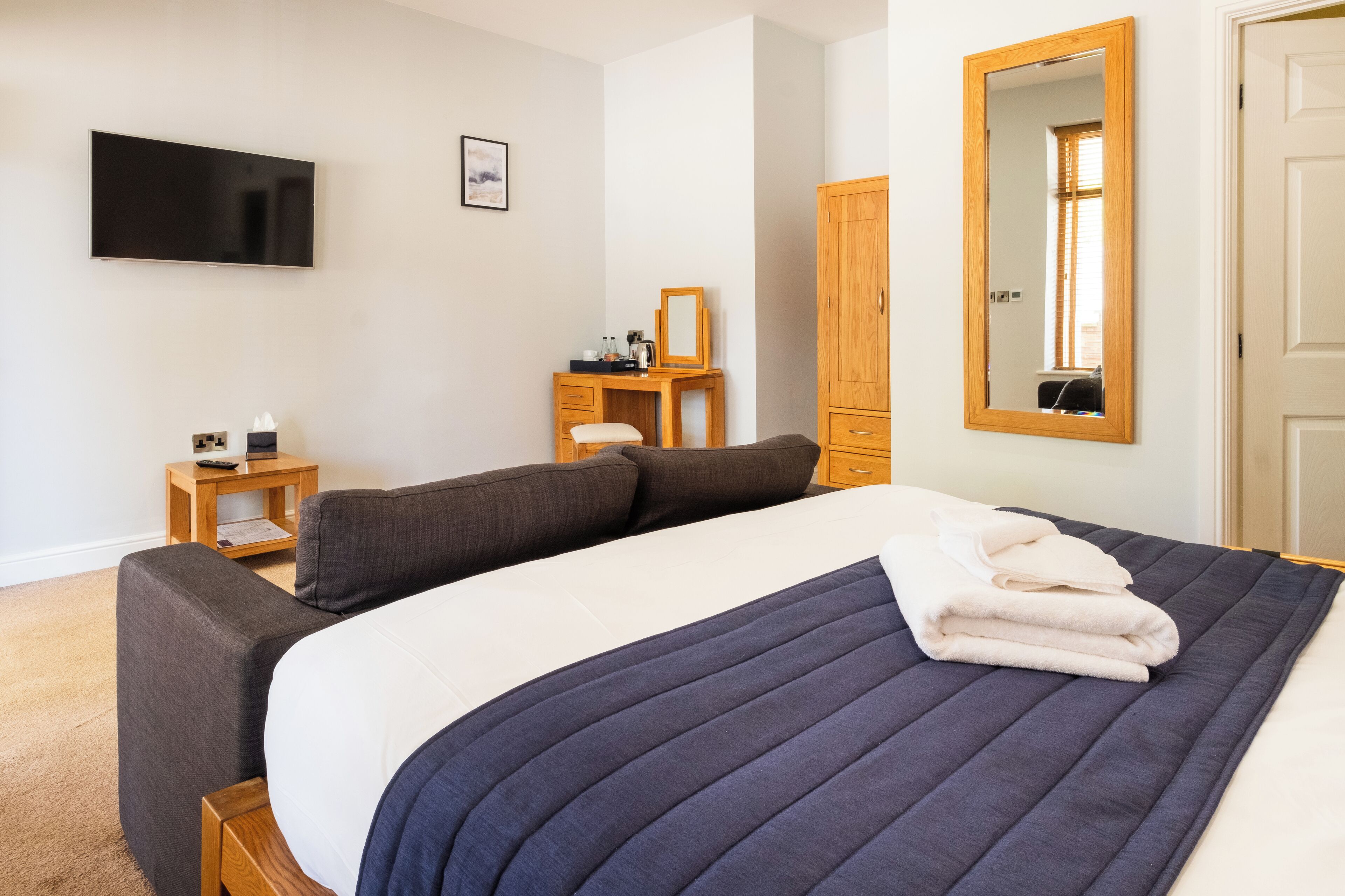 A bedroom with a bed, bedside table, TV, wardrobe, and a mirror.