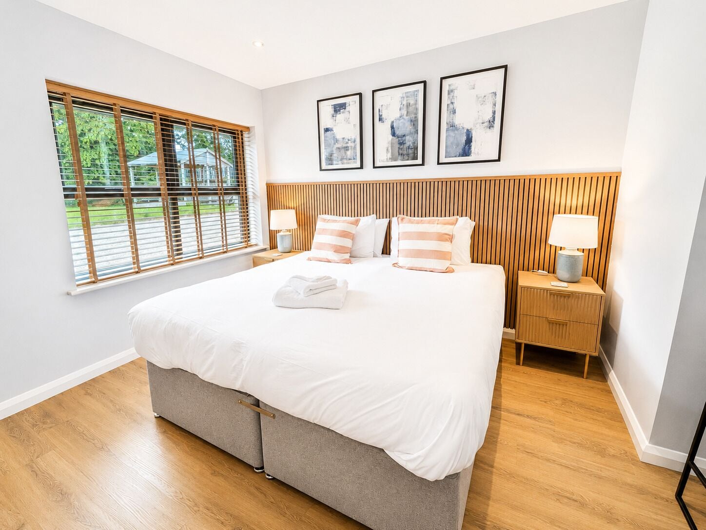 Une chambre d’hôtel moderne avec un grand lit, une tête de lit en bois et une fenêtre équipée de stores.