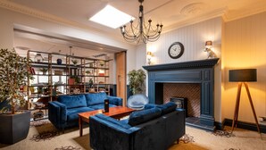 A spacious living room with a blue sofa set, a fireplace, a bookshelf, and a large potted plant. - The Coach House Suffolk (Lowestoft)