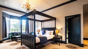 A four-poster bed with a canopy, a sitting area with a chair and a table, and a large window with curtains. - The Coach House Suffolk (Lowestoft)
