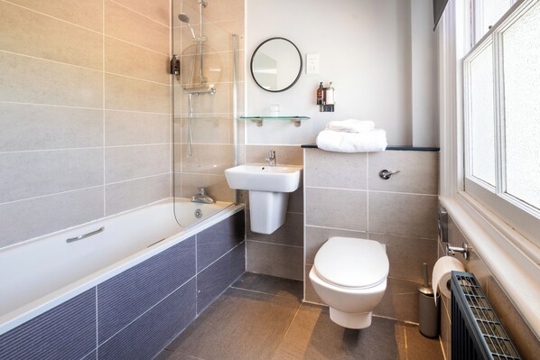 Un baño moderno con bañera, lavabo, inodoro y mampara de cristal.