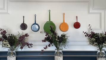 Eine Wand mit mehreren hängenden Töpfen in verschiedenen Farben und ein Kamin mit zwei Blumenvasen.