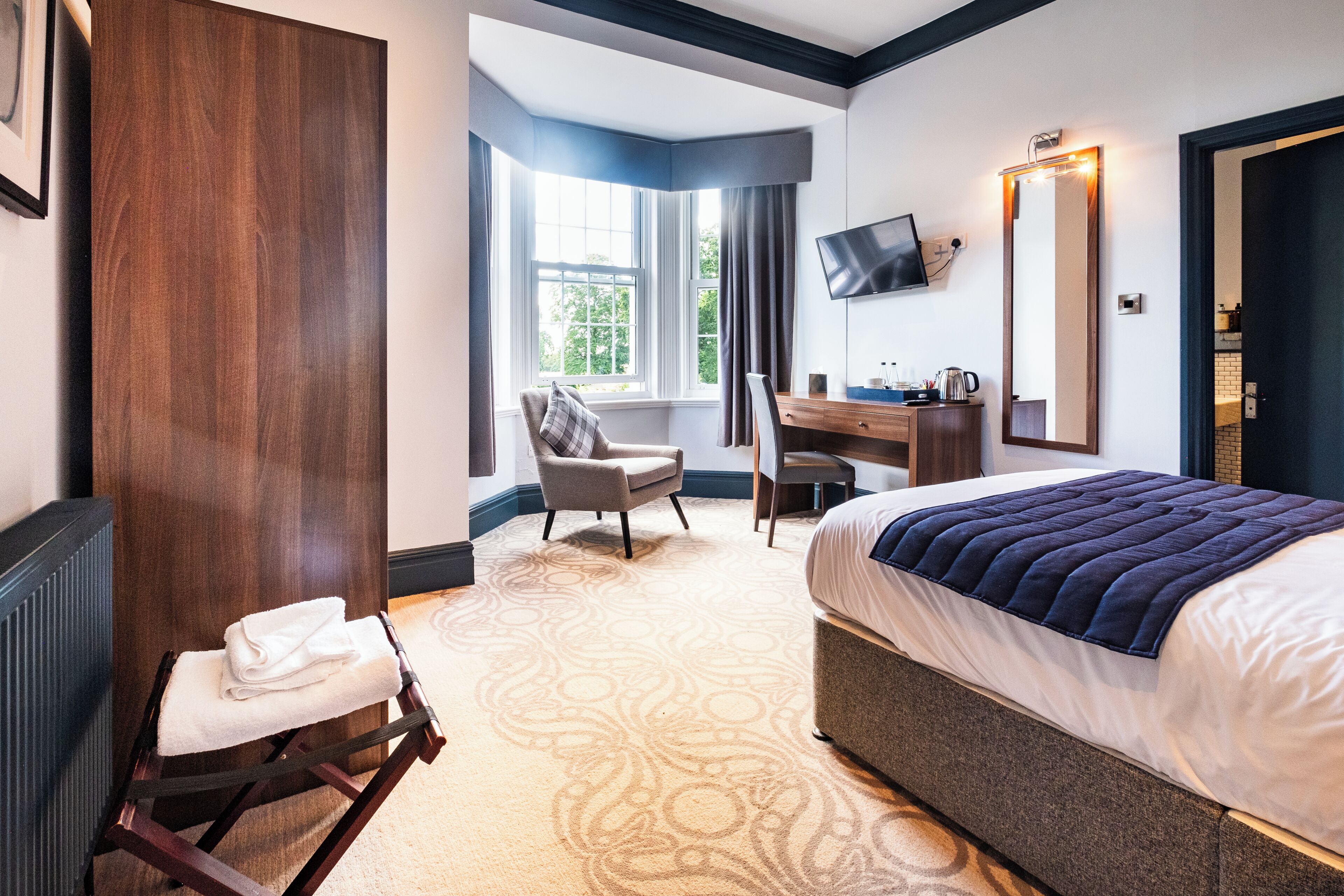 A hotel room with a bed, a desk, a chair, a television, and a large mirror.