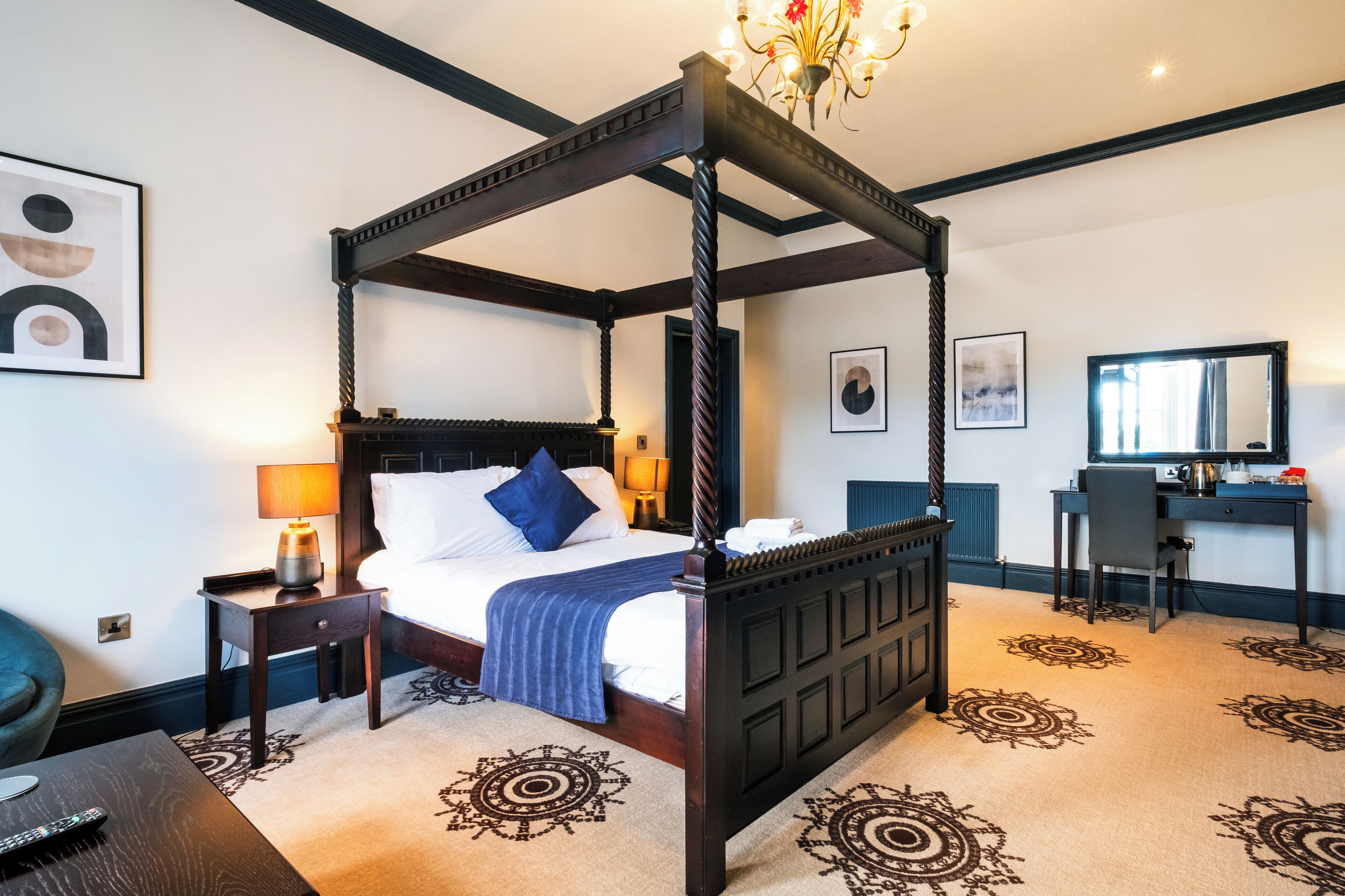 A four-poster bed with a dark wooden frame, a desk with a chair, and a large mirror in a hotel room.