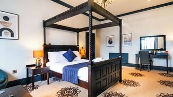 Ein Hotelzimmer mit einem Bett mit Baldachin und dunklem Holzgestell, einem Schreibtisch mit Stuhl und einem großen Spiegel.