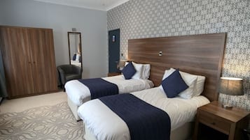 Een hotelkamer met twee bedden, een garderobe, een spiegel en een kamerbreed tapijt met patroon.