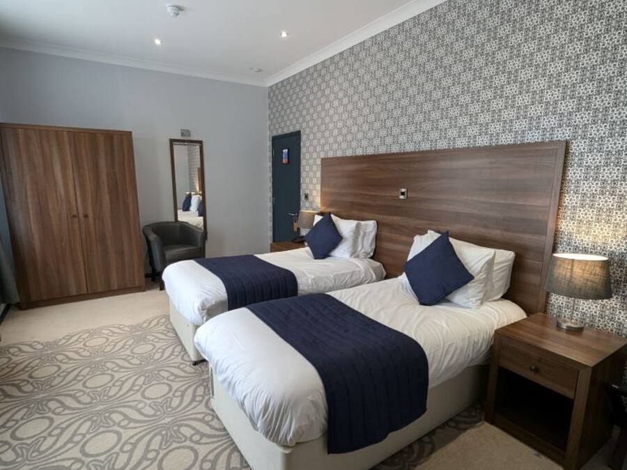 Een hotelkamer met twee bedden, een garderobe, een spiegel en een kamerbreed tapijt met patroon.