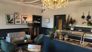 A modern hotel lobby with a chandelier, seating area, and a bar. - The Coach House Suffolk (Lowestoft)