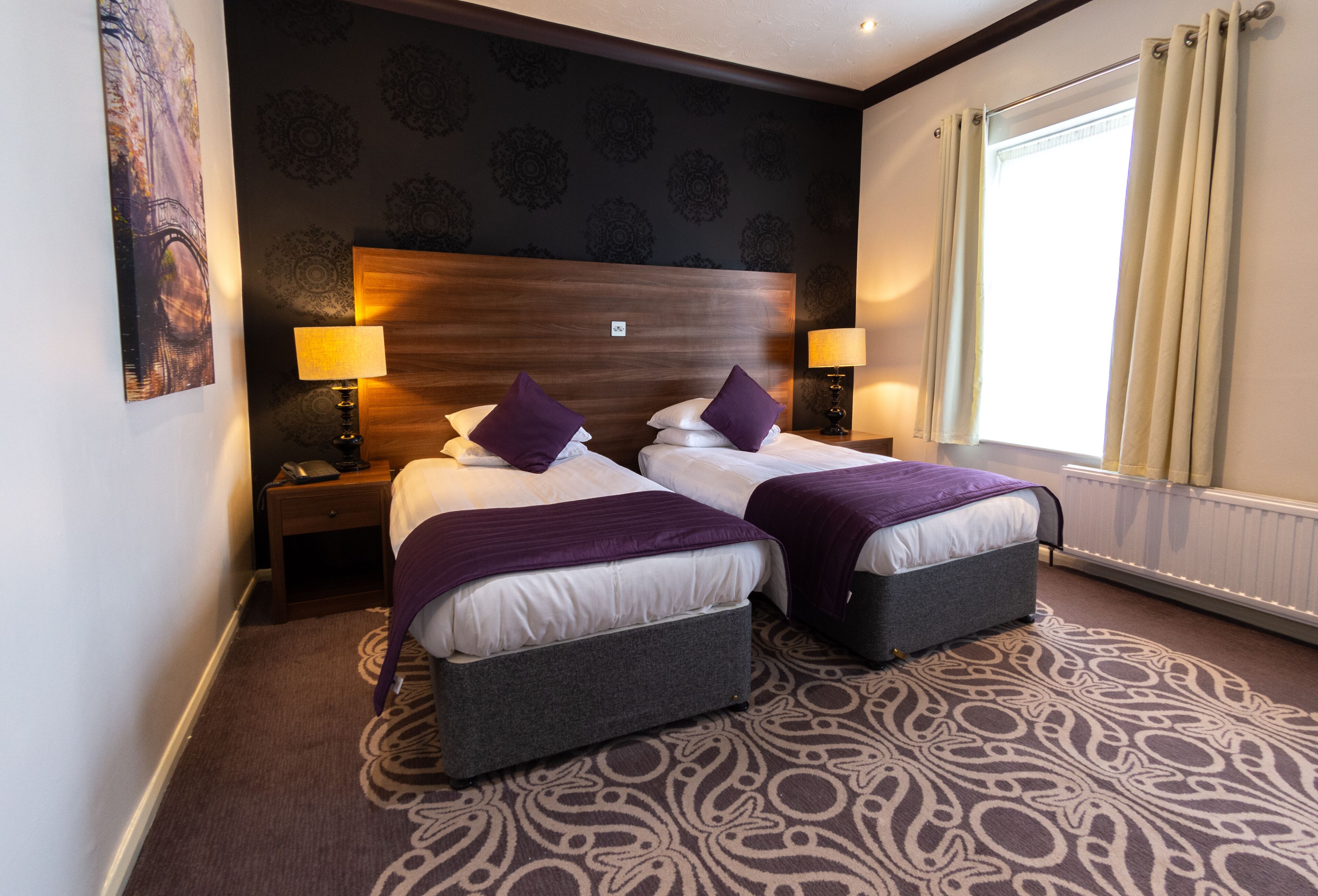 Une chambre d’hôtel avec deux lits, une grande tête de lit, une moquette à motifs et une fenêtre avec des rideaux.