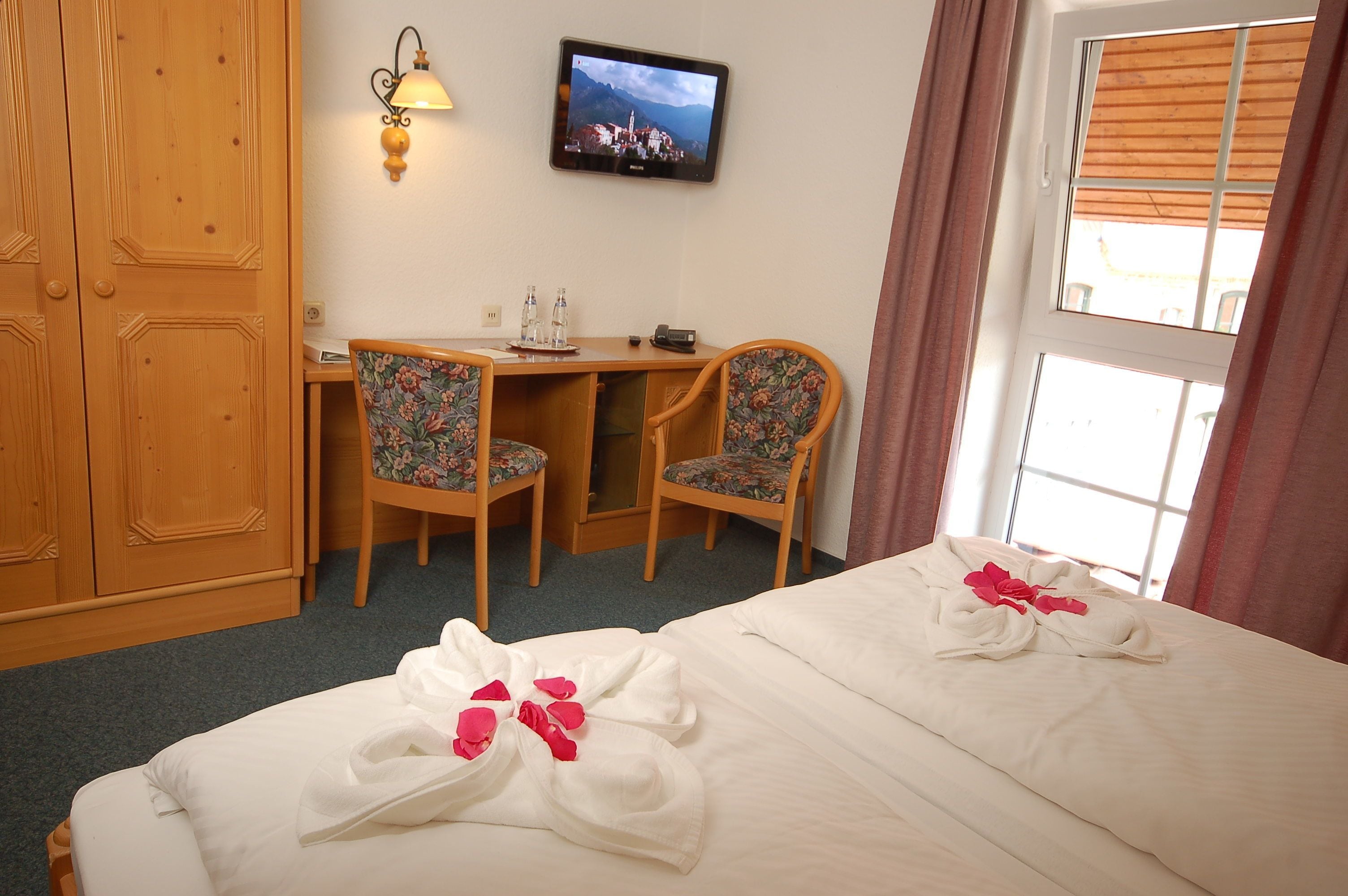 A hotel room with a bed, two chairs, a desk, a television, and a wardrobe.