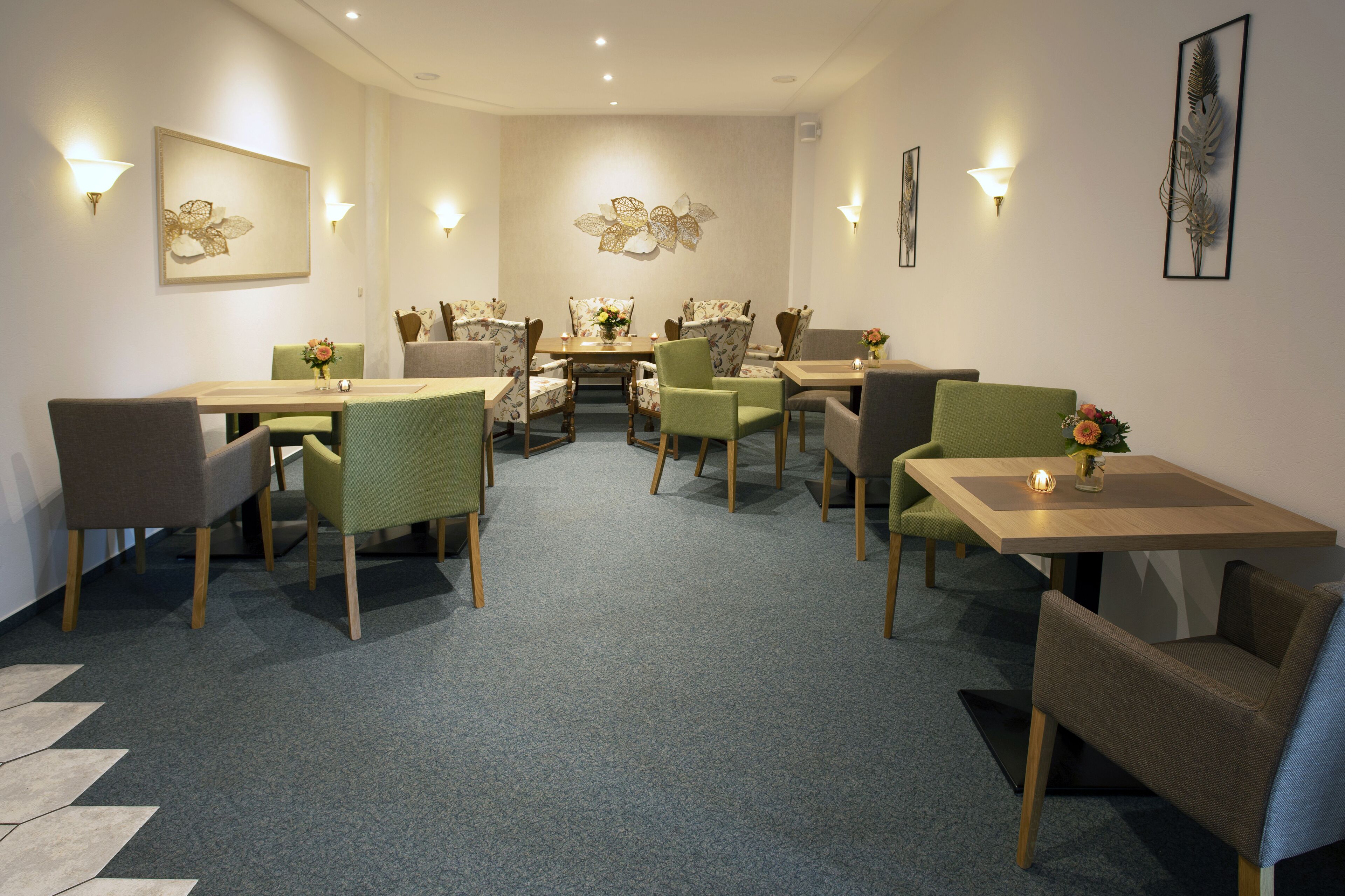 A dining area with multiple tables and chairs, wall-mounted light fixtures, and framed artwork.