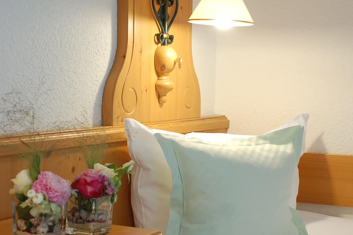 Una cama bien hecha con un cojín verde claro y una mesita de noche de madera con una lámpara y un florero con flores.