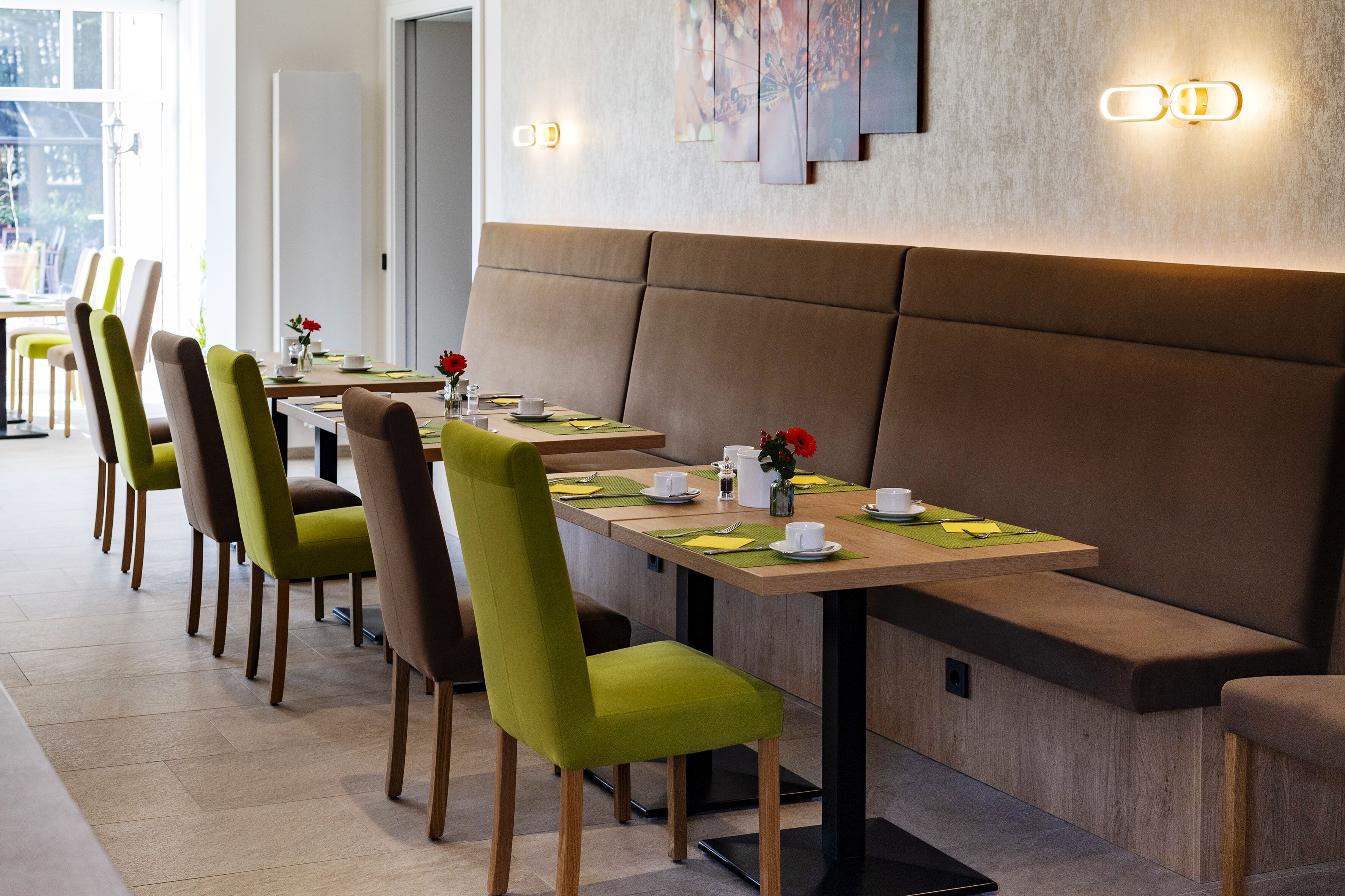 A modern dining area with multiple tables and chairs, a bench, and a wall-mounted light fixture.