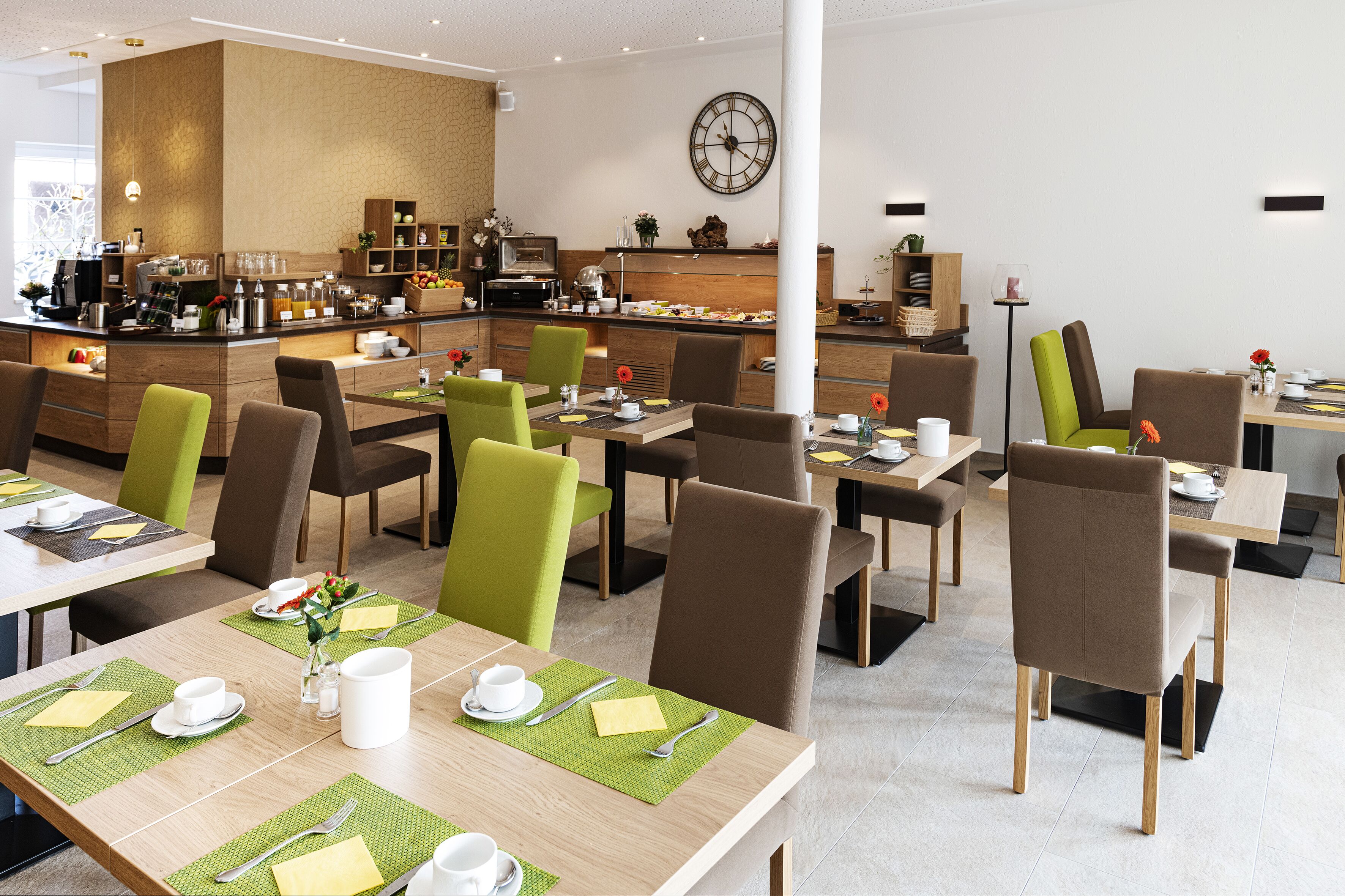 A modern dining area with multiple tables and chairs, a bar area with various food and drink options, and a large clock on the wall.