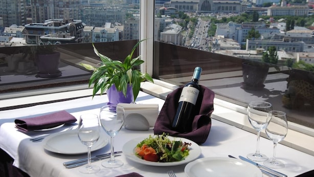Ein Esstisch gedeckt mit Tellern, Besteck und einer Weinflasche, mit Blick auf die Stadt durch ein Fenster.