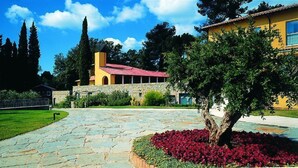 Une cour avec un chemin en pierre, un bâtiment jaune avec un toit rouge et un arbre aux fleurs rouges.