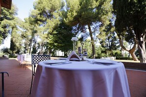 An outdoor table set with a white tablecloth, surrounded by trees. - Relais Villa Matarazzo (Gradara)