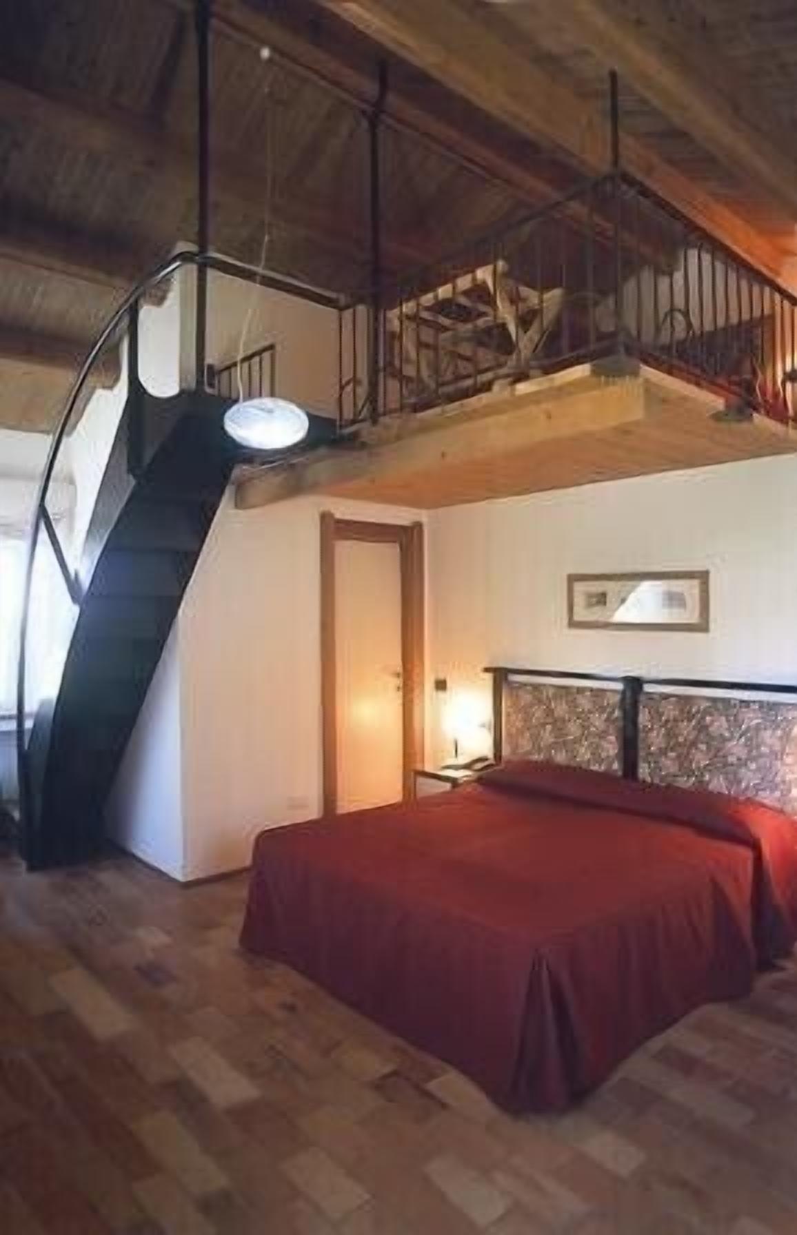 Een slaapkamer met een bed, een nachtkastje, een lamp, een houten trap en een ingelijst schilderij aan de muur.