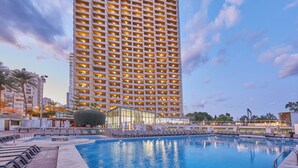 Un hotel moderno de gran altura con piscina, tumbonas y fachada de vidrio.