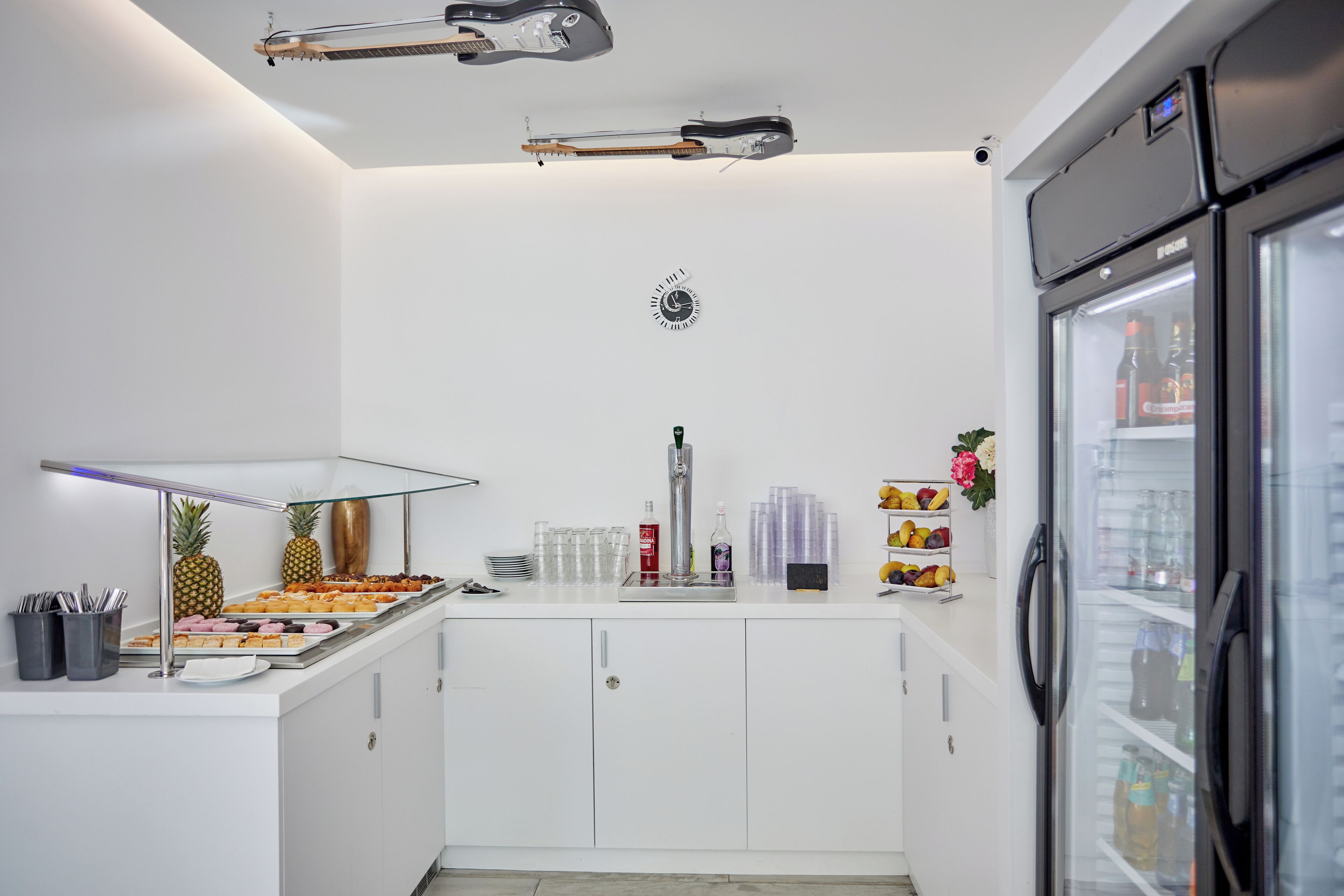 A modern kitchen with white cabinets, a stainless steel refrigerator, and a glass display case with food items.