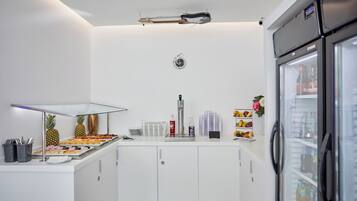 A modern kitchen with white cabinets, a stainless steel refrigerator, and a glass display case with food items.