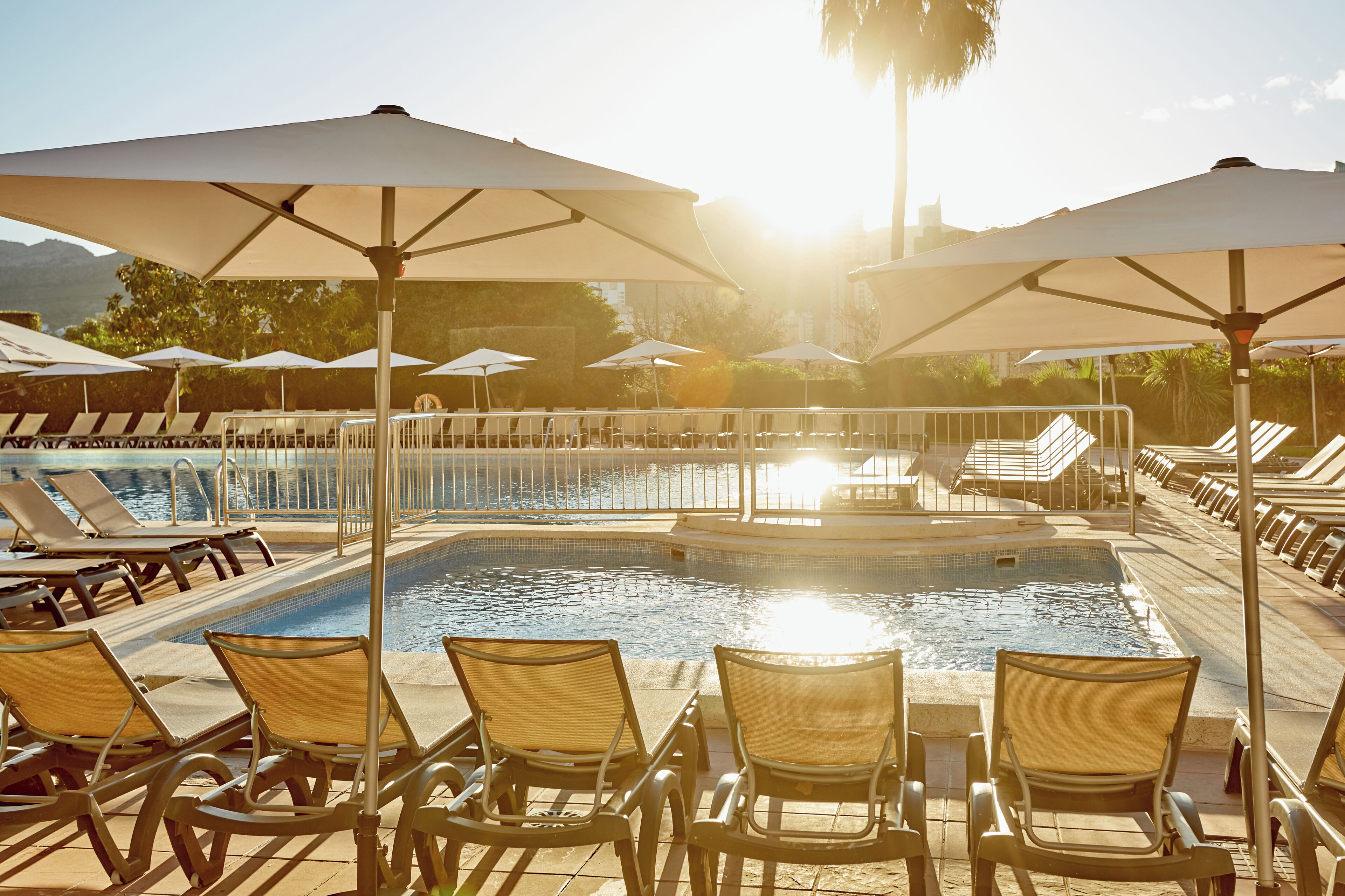 A poolside area with sun loungers and umbrellas, a small pool, and a fountain.