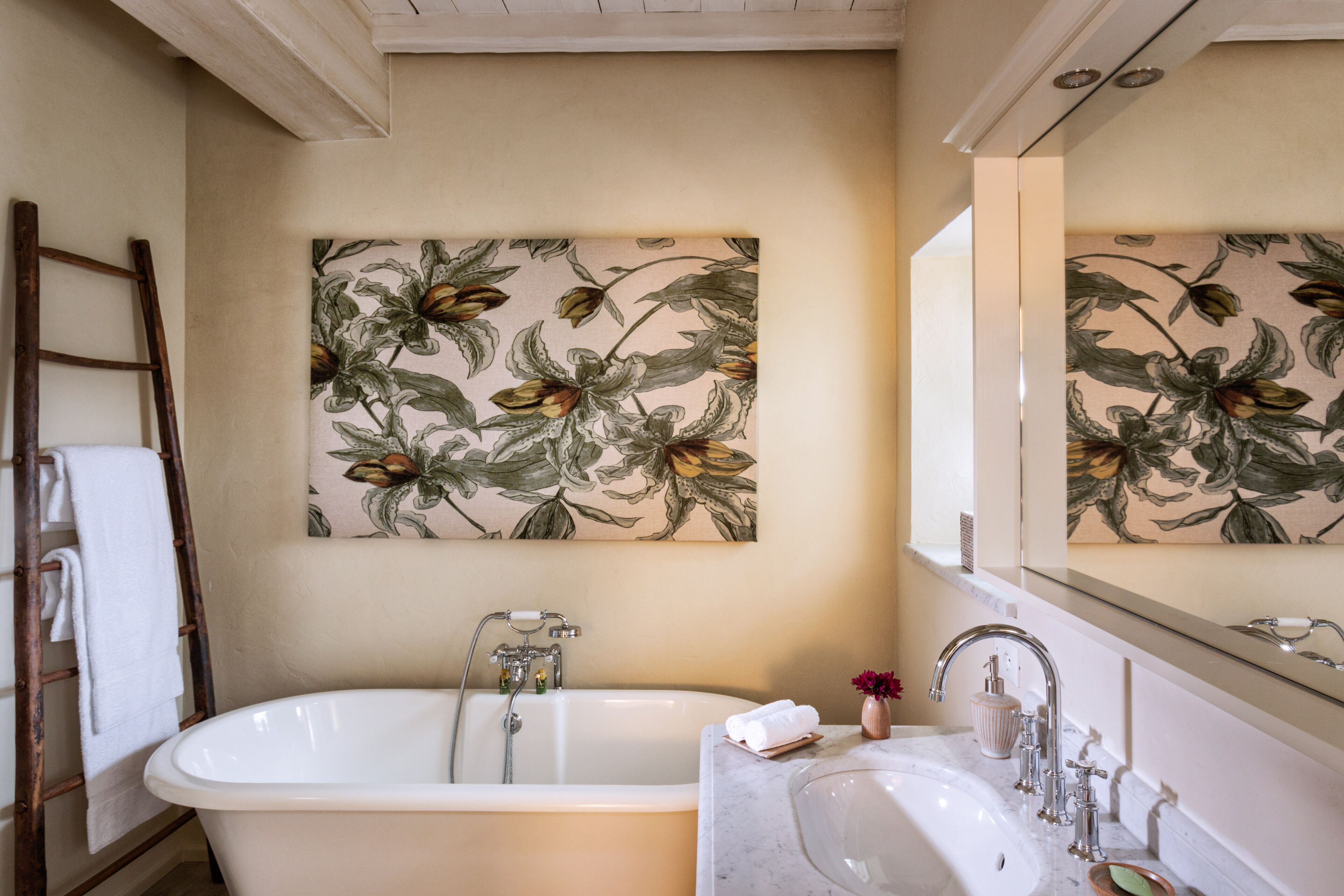 Un baño con una bañera independiente, un lavabo con espejo y un mural floral.