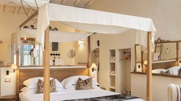 Un dormitorio con cama con dosel, vigas de madera en el techo, un espejo grande y un sillón a rayas.