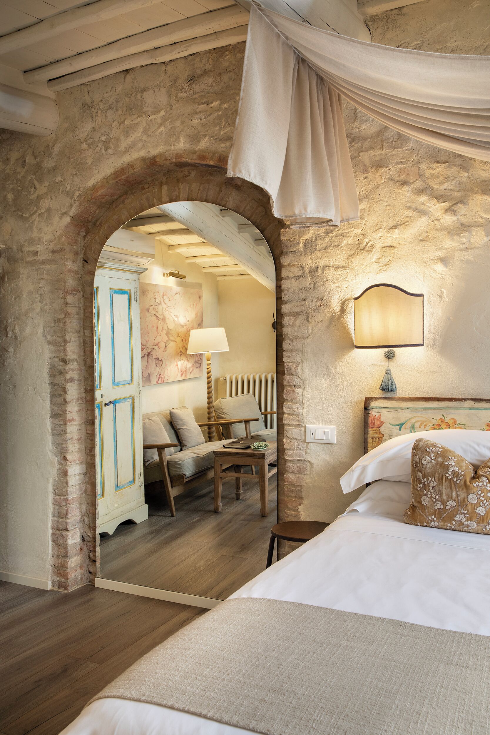 Un dormitorio con una cama grande, una zona de estar con una lámpara y vistas a través de un arco.