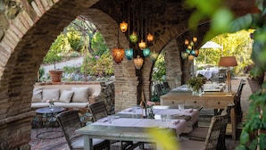 Une terrasse extérieure agrémentée d’arches en briques, de meubles en osier et de lanternes suspendues.