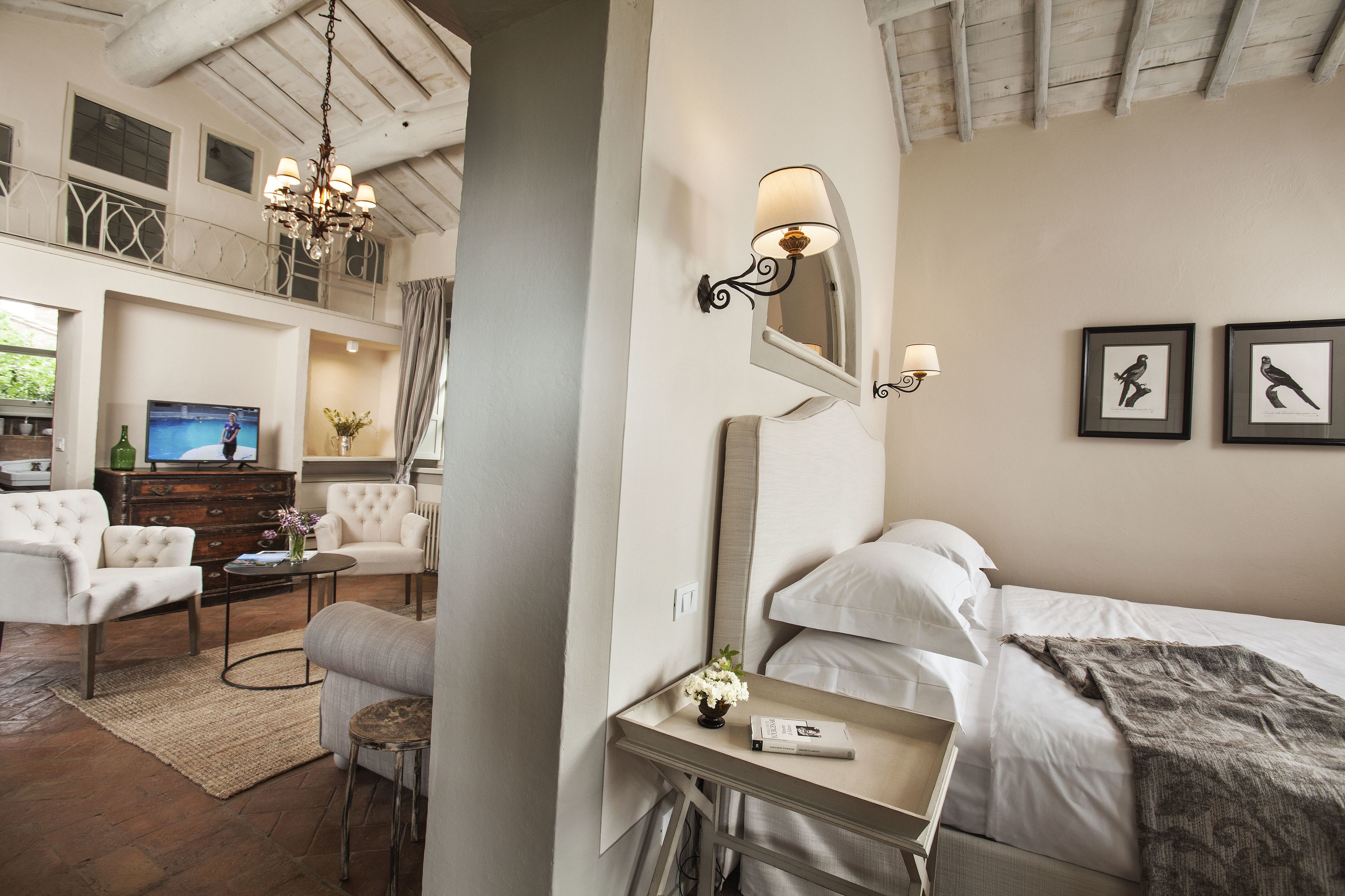 Una habitación de hotel con una cama, un escritorio con lámpara, televisi ón y un área de estar con sofá y sillón.