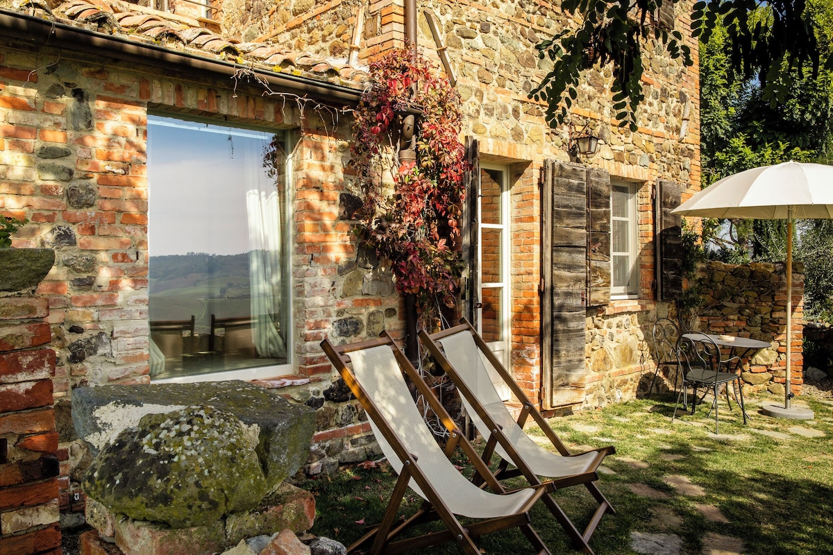 A stone building with a glass door leading to a patio area with two lounge chairs and a table.